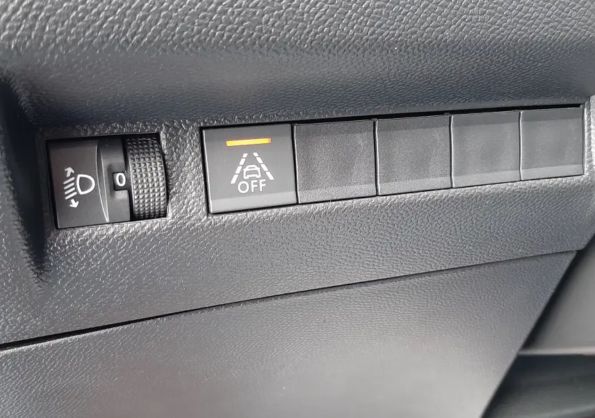 Gros plan sur les commandes de réglage des phares et d'alerte de maintien de voie dans l'habitacle noir du Peugeot 2008 gris.
