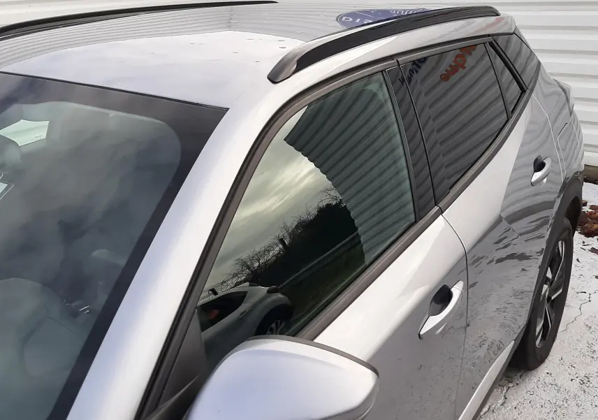 Vue rapprochée côté gauche arrière du Peugeot 2008 gris 2021 avec toit noir et barres de toit noires.