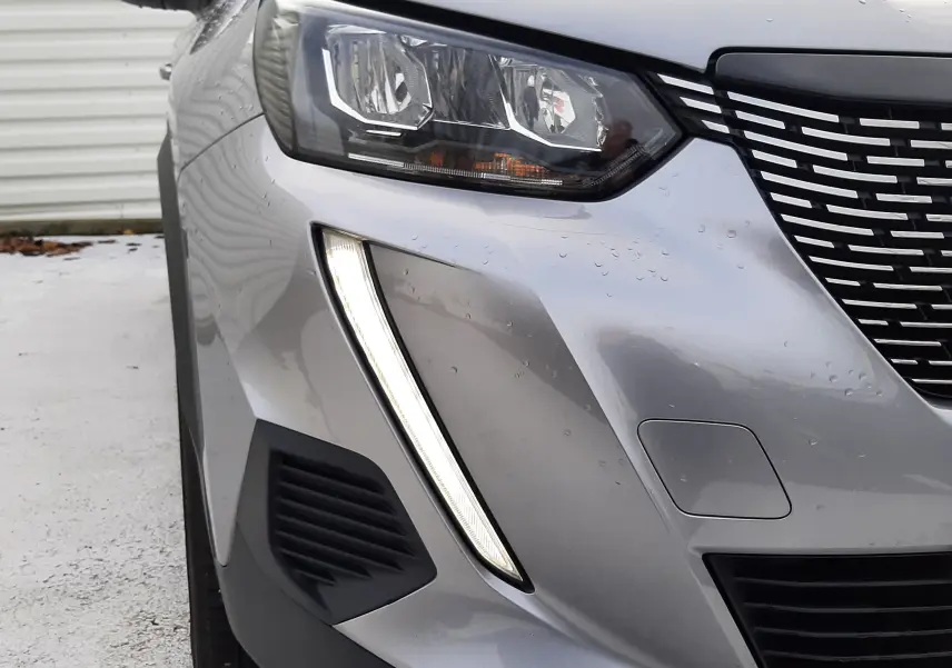 Gros plan sur l'avant gauche gris du Peugeot 2008 2021, mettant en valeur son phare et sa signature lumineuse verticale LED.
