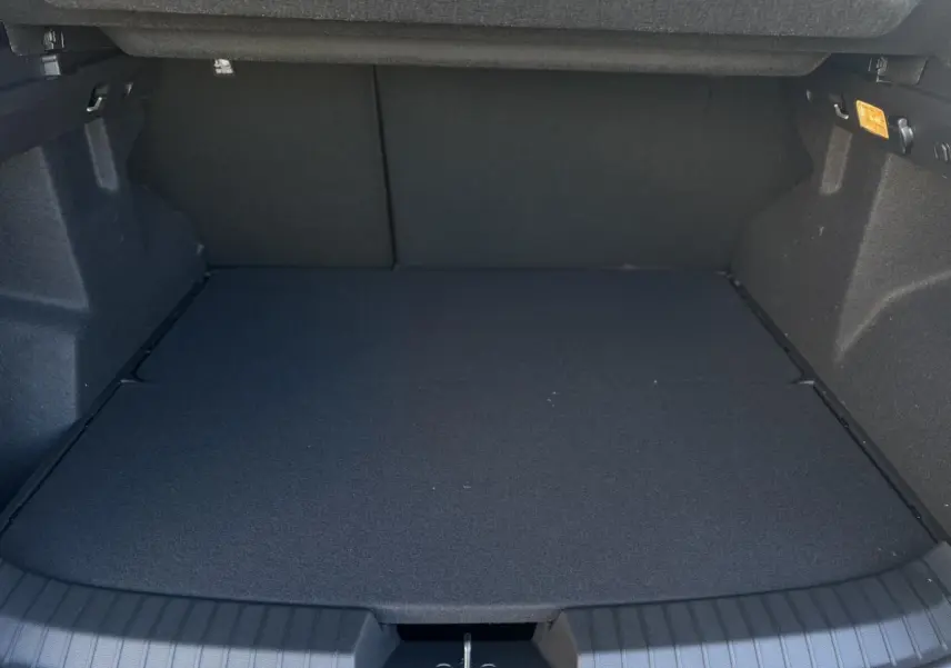 Coffre ouvert vu de face du Dacia Duster blanc Glacier, montrant un espace de chargement plat et spacieux.