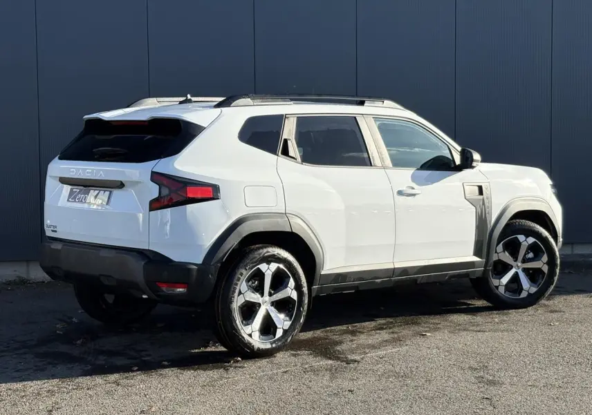 Vue 3/4 arrière droite du Dacia Duster blanc Glacier avec jantes alliage et barres de toit noires.