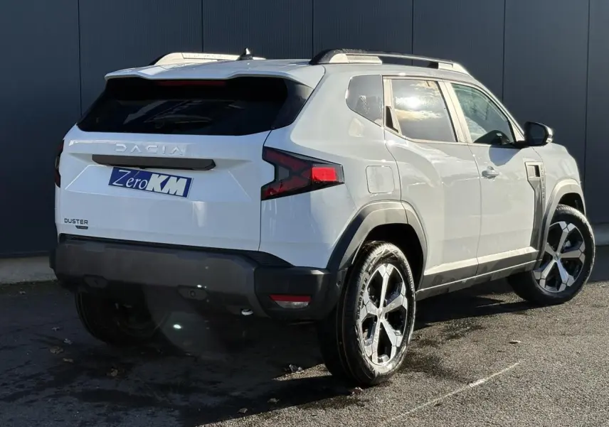 Vue 3/4 arrière droite du Dacia Duster blanc Glacier 2026 avec jantes alliage et barres de toit noires.