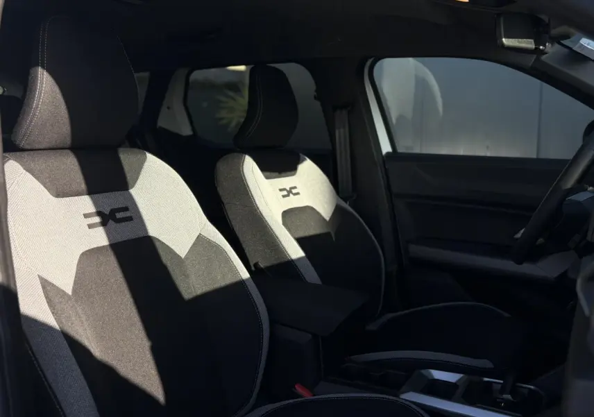 Vue intérieure côté gauche montrant les sièges avant noirs et gris avec logo Dacia sur appuie-tête.