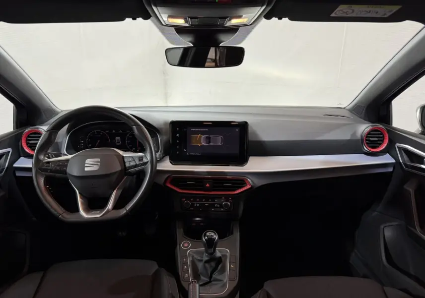 Intérieur SEAT Ibiza 1.0 TSI 110 FR 2024 vu de face, tableau de bord noir avec touches rouges et volant multifonctions cuir alu.