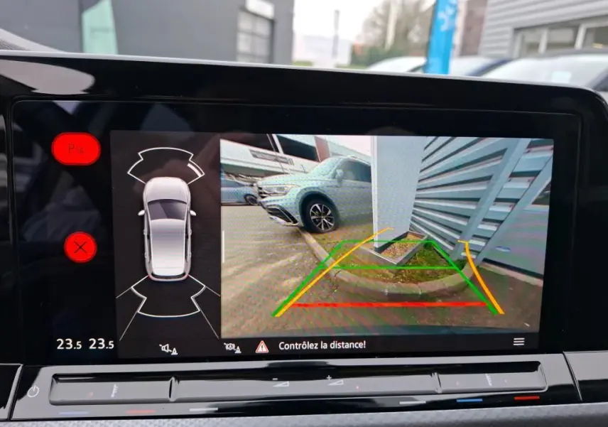Vue écran caméra de recul d'une Volkswagen Golf gris 2022, affichant les lignes de guidage et un obstacle côté droit.