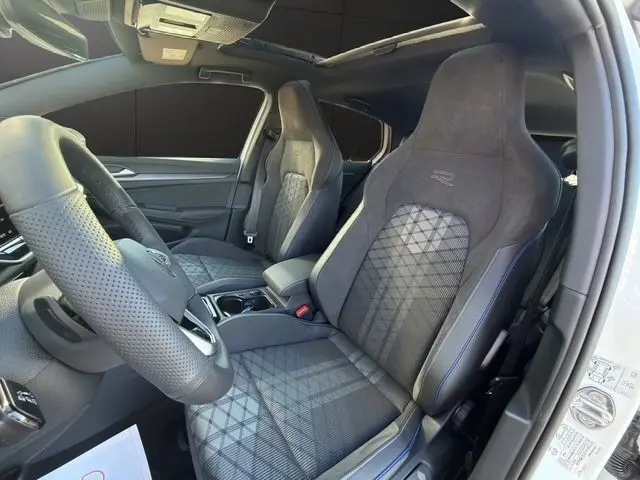 Vue intérieure côté conducteur de la Volkswagen Golf 2.0 TDI R-Line 2025, sièges sport noirs avec surpiqûres bleues et volant cuir.