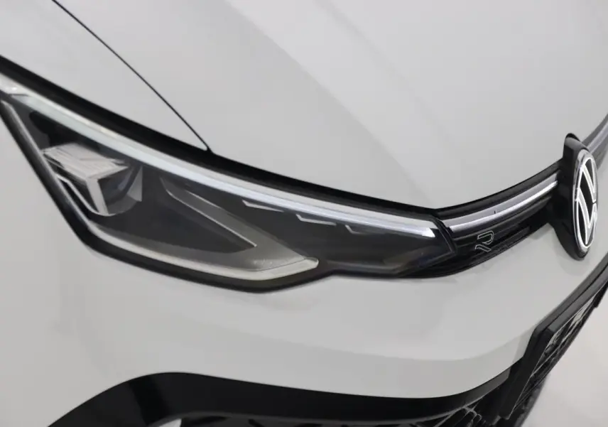 Gros plan sur le phare avant gauche blanc d'une Volkswagen Golf 2.0 TDI R-Line avec logo et calandre noire.
