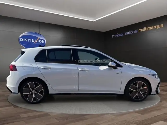 Vue latérale droite d'une Volkswagen Golf blanche 2025 en finition R-Line avec toit panoramique dans un showroom.