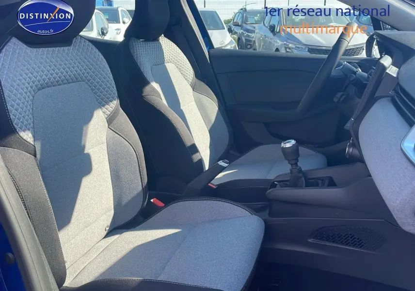 Intérieur avant de la Renault Clio V bleu iron, sièges tissu bicolore gris et noir, volant multifonction et boîte manuelle visible.