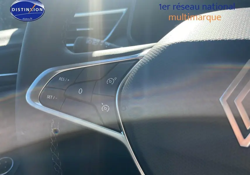 Gros plan sur le volant multifonction noir de la Renault Clio V bleu iron, mettant en valeur les commandes de régulateur de vitesse.