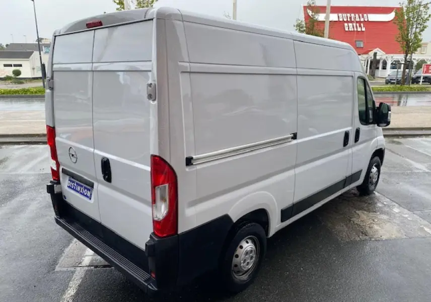Vue 3/4 arrière droite d'un Opel Movano Fourgon blanc 2023 stationné sur sol humide, avec portes arrière fermées.