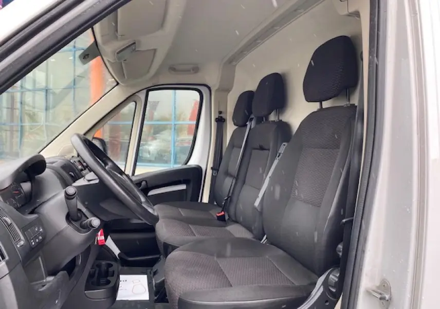 Vue intérieure côté conducteur de l'Opel Movano Fourgon blanc 2023 avec sièges tissu noir et tableau de bord simple.