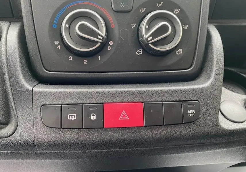 Gros plan sur les commandes de climatisation et les boutons de sécurité du tableau de bord du fourgon Opel Movano blanc.