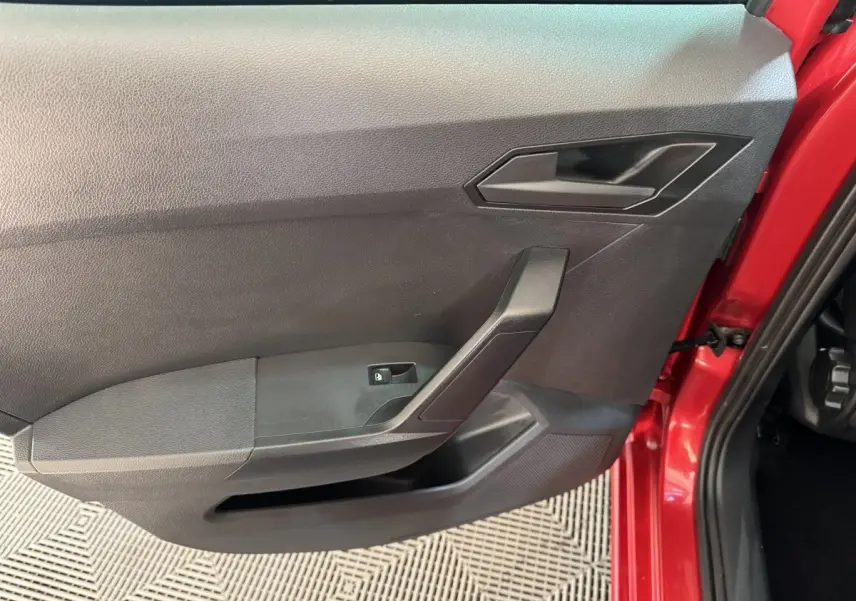 Vue intérieure côté gauche de la porte avant rouge d'une SEAT IBIZA 1.0 TSI 110 FR avec poignée noire et bouton de lève-vitre.