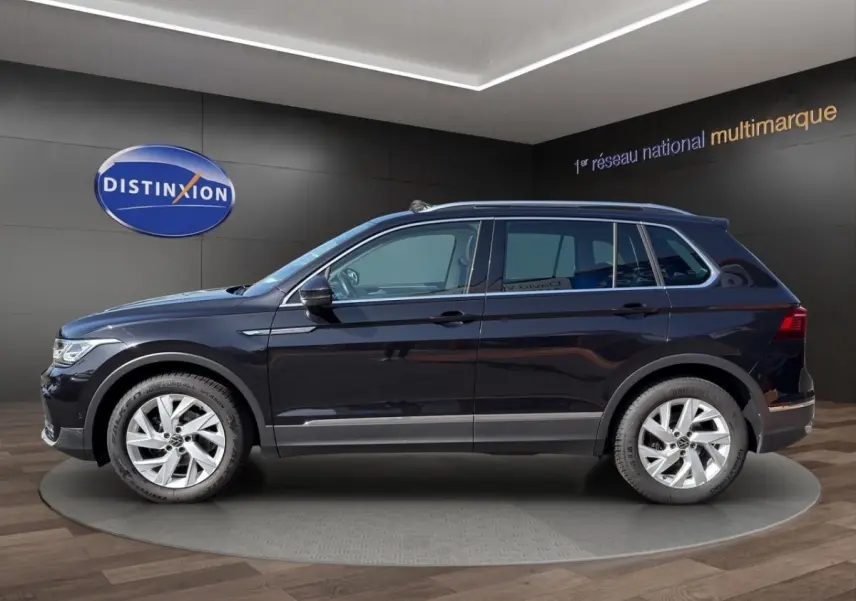 Profil droit d’un Volkswagen Tiguan noir 2022, finition Elegance, avec jantes alliage et barres de toit chromées.