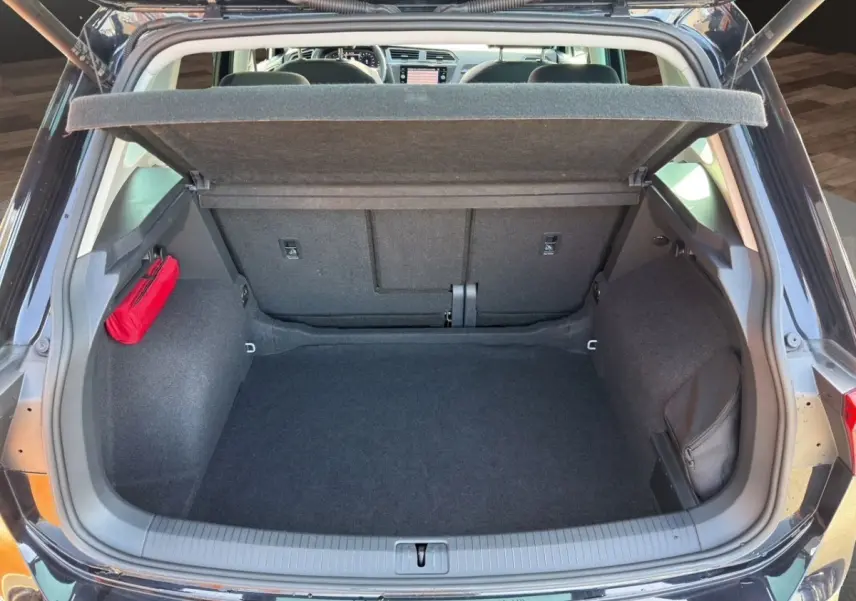 Coffre ouvert vu de l'arrière d'un Volkswagen Tiguan noir, avec tapis noir et rangement latéral rouge et noir.