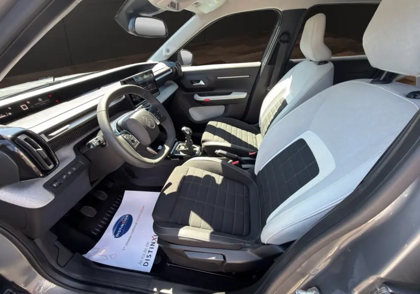 Vue intérieure côté conducteur de la Citroën C3 2025 gris foncé, sièges bicolores et tableau de bord digital.