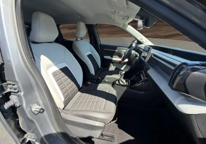 Intérieur avant droit de la Citroën C3 2025 gris foncé, sièges bi-ton gris clair et noir, tableau de bord moderne avec écran tactile.