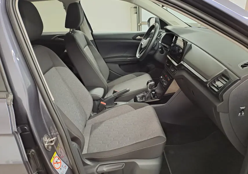 Vue intérieure côté gauche du Volkswagen T-Cross gris cendré 2025, montrant les sièges tissu et le tableau de bord moderne.