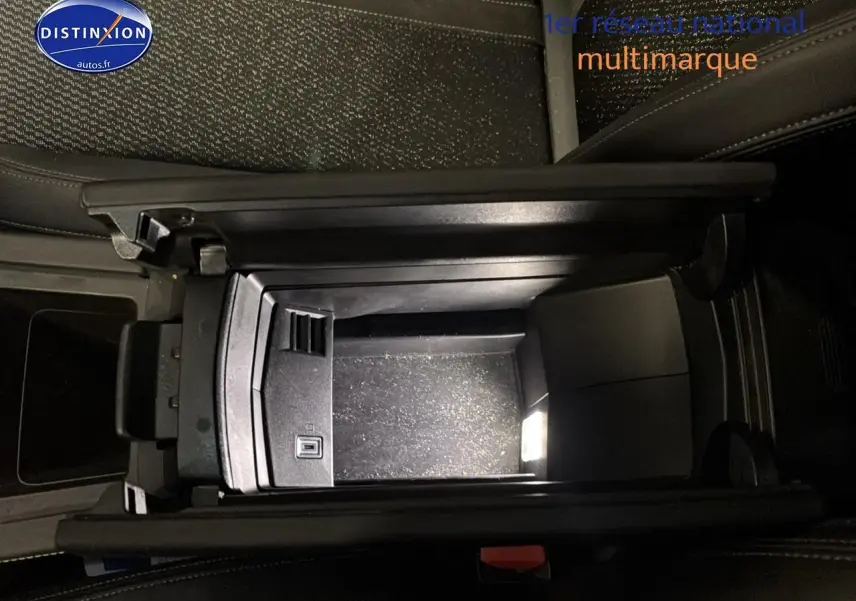 Vue plongeante sur l'accoudoir central ouvert de la Peugeot 408 Hybrid 145 GT gris sélénite, montrant le rangement intérieur.