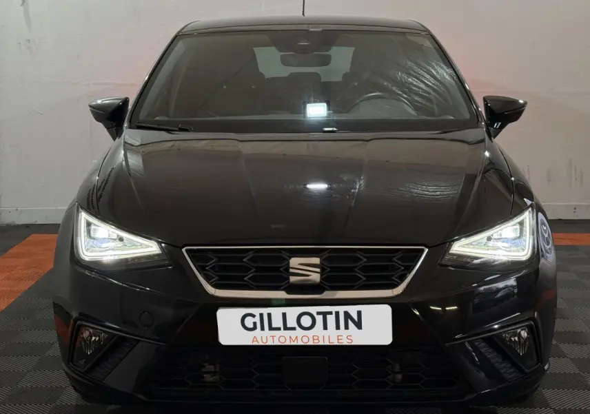 Vue frontale d'une SEAT Ibiza 1.0 TSI 110 FR noire avec phares LED allumés dans un showroom.