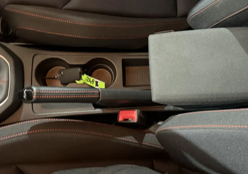 Vue plongeante sur la console centrale noire de la SEAT Ibiza 2024 avec frein à main cuir et coutures rouges visibles.