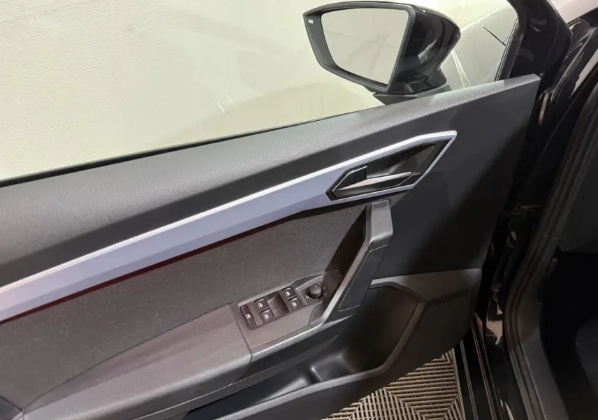 Vue intérieure de la porte avant gauche noire d'une SEAT IBIZA 1.0 TSI 110 FR avec commandes électriques et rétroviseur intégré.