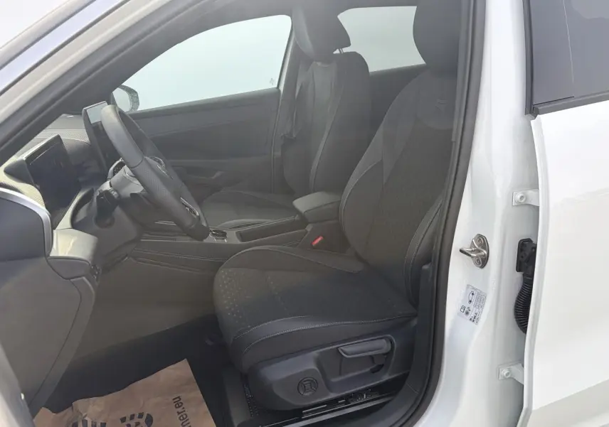 Vue intérieure côté conducteur du Volkswagen T-Roc blanc pur, montrant les sièges sport R-Line en tissu noir et le volant multifonction en cuir.