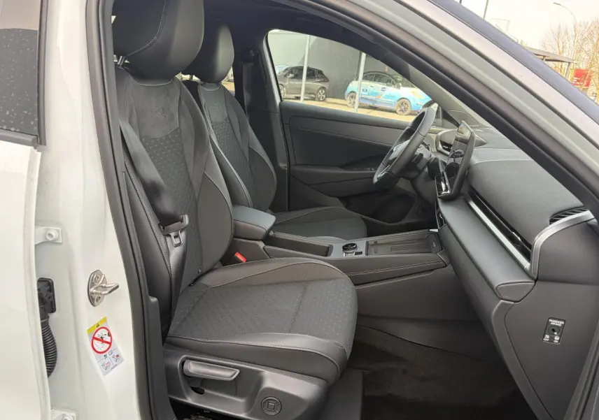 Vue intérieure côté conducteur du Volkswagen T-Roc blanc pur, mettant en valeur les sièges sport R-Line en tissu gris foncé.