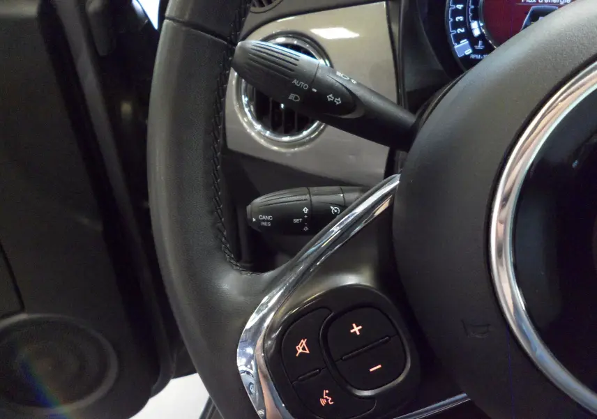 Gros plan sur le volant cuir noir de la Fiat 500 hybride 2021 avec commandes intégrées et aérateur gris Electroclash.