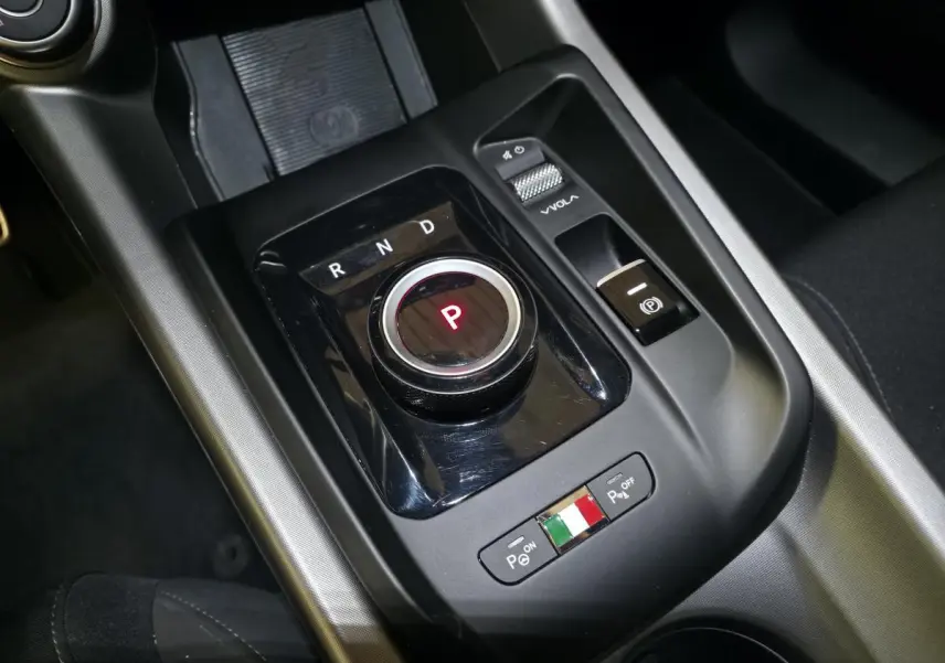 Gros plan sur la console centrale noire de l'Alfa Romeo Tonale avec sélecteur rotatif de vitesse et commande de volume.
