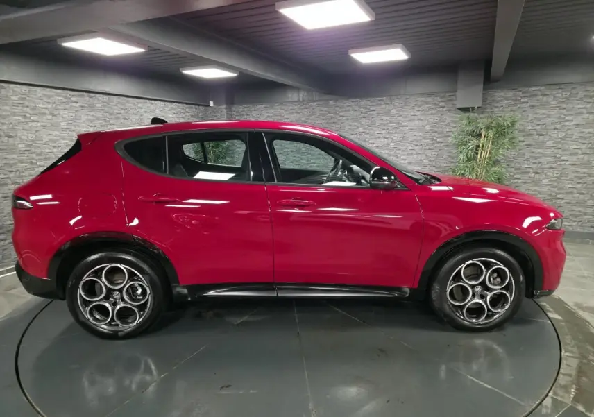 Vue de profil côté gauche d'un Alfa Romeo Tonale rouge avec jantes alliage 18 pouces et détails noirs brillants.