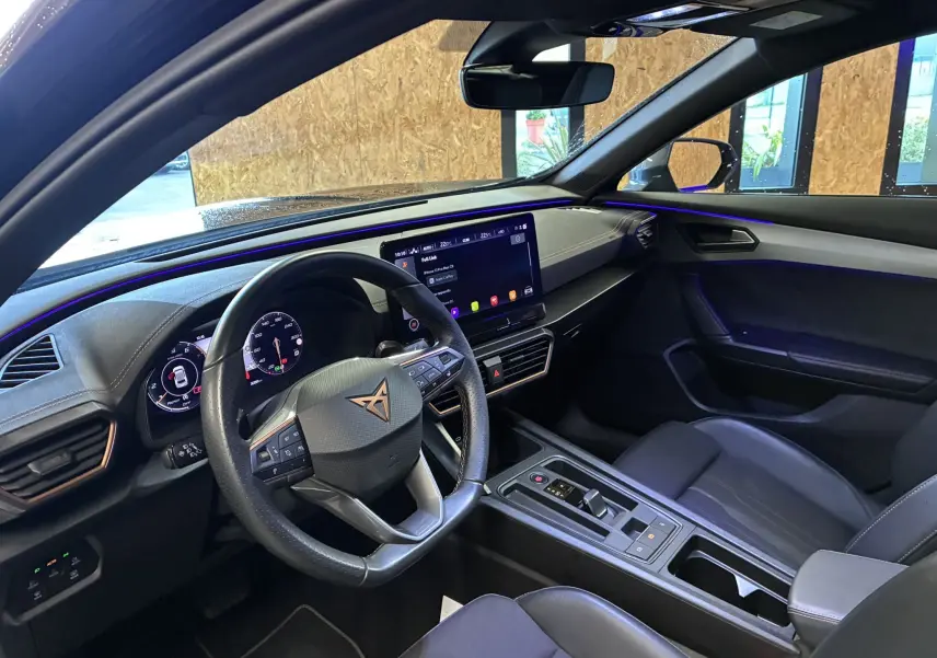 Vue intérieure côté conducteur du CUPRA Formentor noir 2023, mettant en valeur le tableau de bord digital et l'ambiance lumineuse bleue.