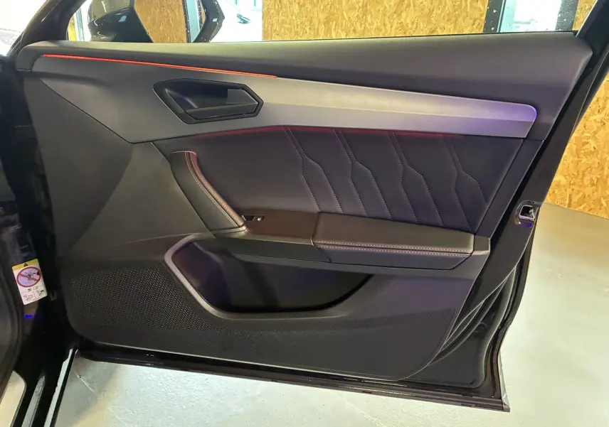 Vue intérieure côté gauche de la porte noire du CUPRA Formentor 1.4 E-HYBRID 2023 avec surpiqûres et bandeau métallique.