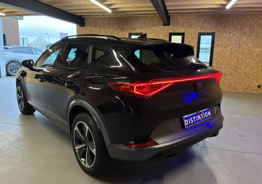 Vue 3/4 arrière droite d’un CUPRA Formentor noir 2023 avec feux arrière allumés dans un garage.