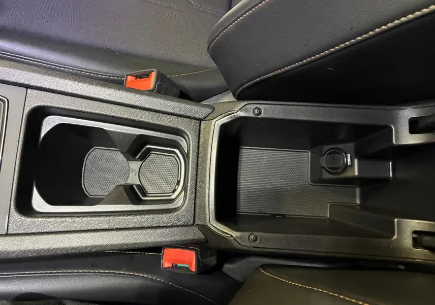 Vue rapprochée de la console centrale noire du CUPRA Formentor 1.4 E-HYBRID 2023 avec porte-gobelets et prise 12V.