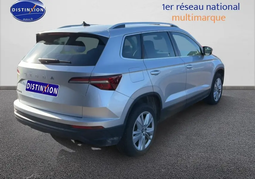 Vue 3/4 arrière droite d'un Skoda Karoq gris avec barres de toit et feux arrière LED sur fond neutre.