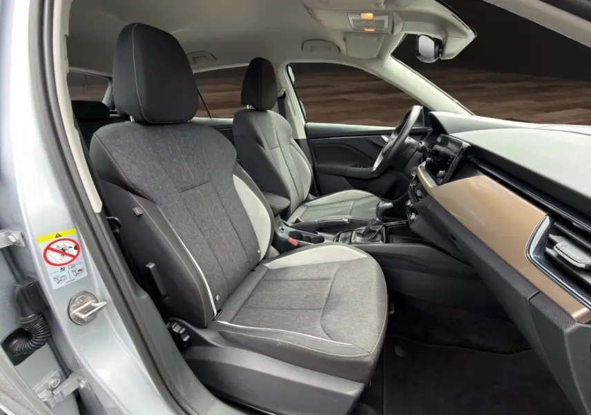 Vue intérieure côté conducteur du Skoda Kamiq 2023 gris clair, montrant sièges tissu bicolore et tableau de bord bois clair.