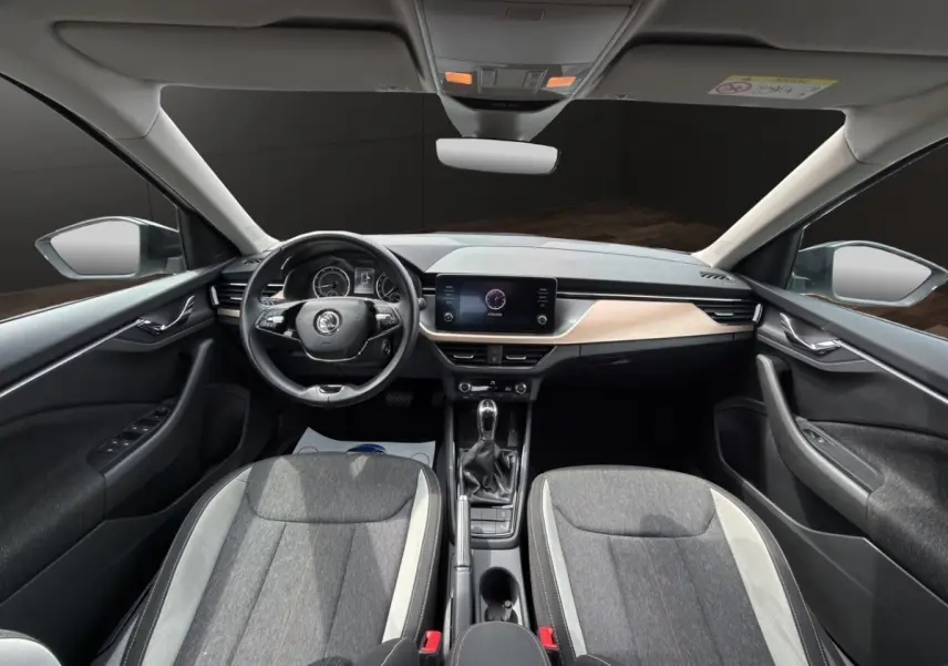 Vue avant intérieure du Skoda Kamiq 2023 avec tableau de bord clair, volant cuir multifonctions et sièges bi-ton gris.