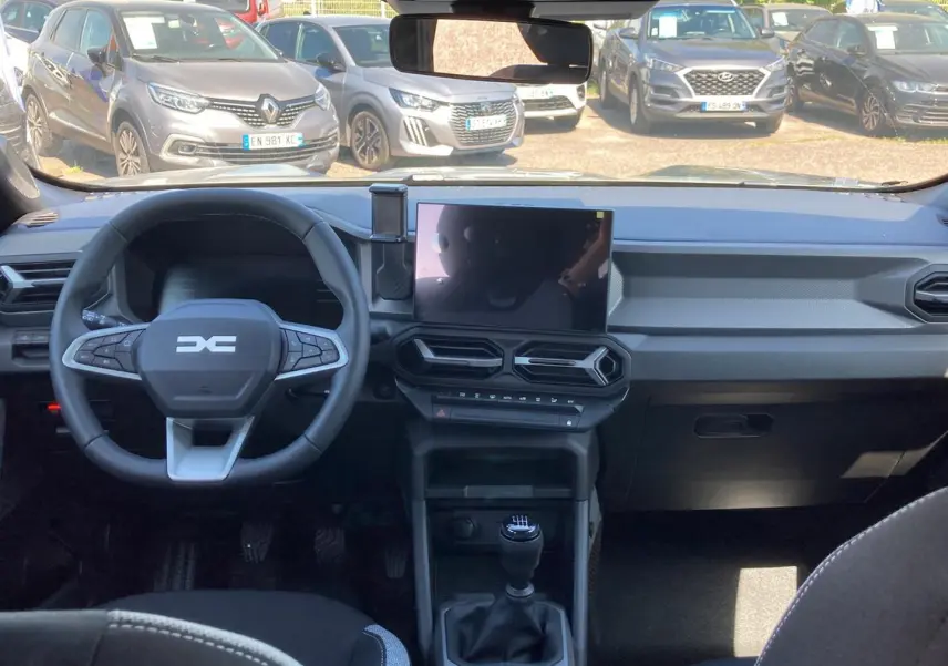 Vue intérieure avant du tableau de bord du Dacia Duster gris schiste 2026 avec volant multifonction et écran tactile central.