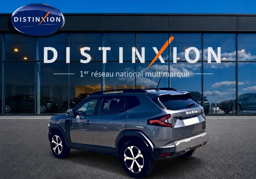 Vue 3/4 arrière droite du Dacia Duster gris schiste 2026 stationné devant une vitrine Distinxion.