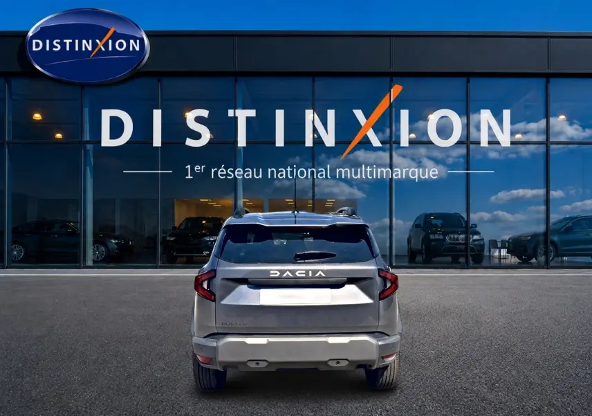 Vue arrière d'un Dacia Duster gris schiste 2026 garé devant une vitrine avec logo Distinxion.