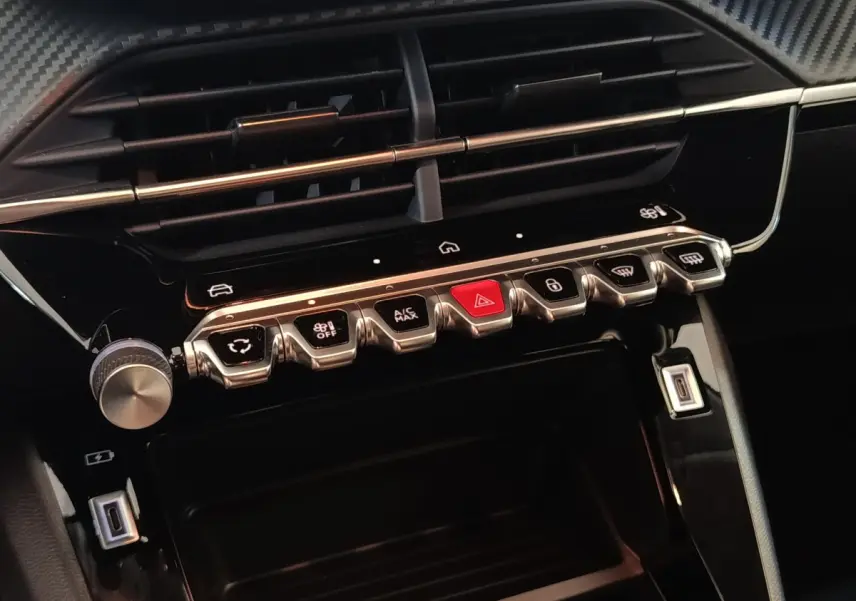 Gros plan sur la console centrale noire du Peugeot 208 Hybrid 2025, avec boutons de commande et prises USB visibles.