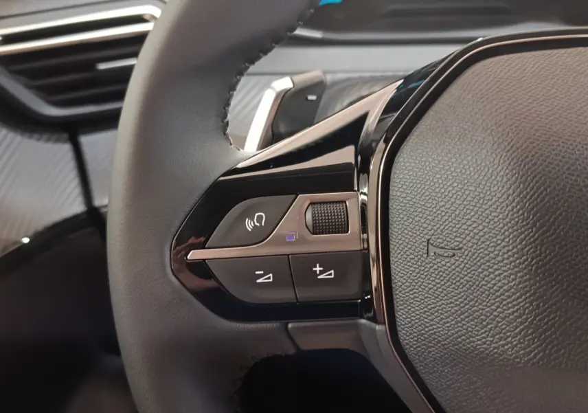 Gros plan sur le volant cuir noir de la Peugeot 208 Hybrid 2025, avec commandes multifonctions et finition brillante.