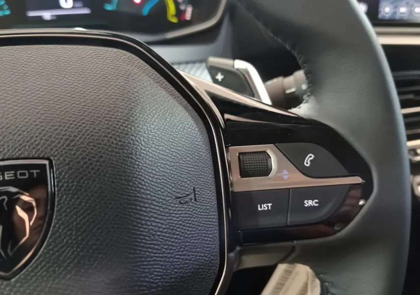 Gros plan sur le volant cuir noir de la Peugeot 208 Hybrid 2025, avec commandes multifonctions côté droit visibles.