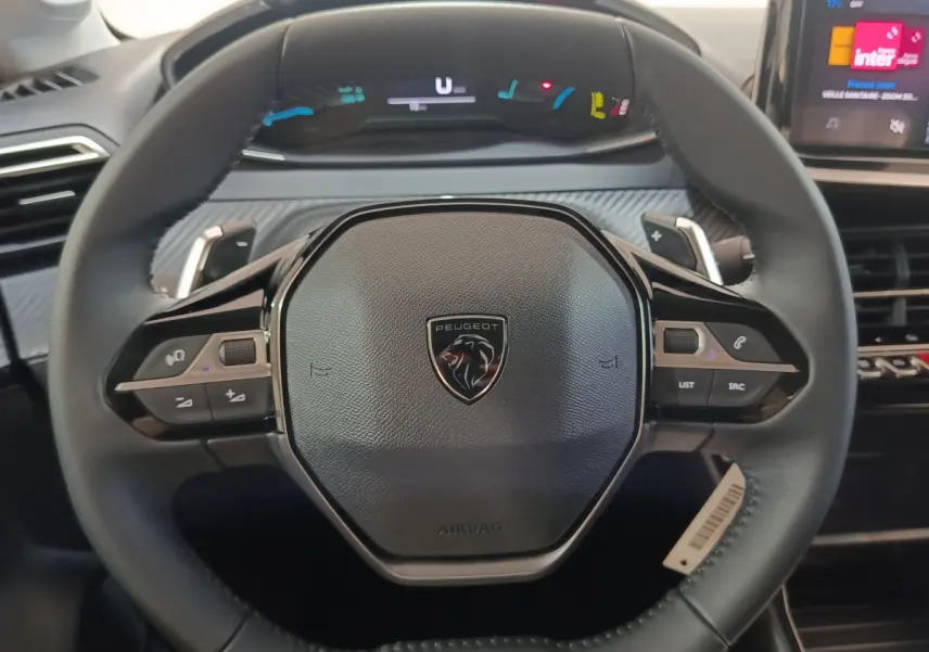 Vue rapprochée du volant cuir multifonctions de la Peugeot 208 Hybrid gris clair avec tableau de bord numérique en arrière-plan.