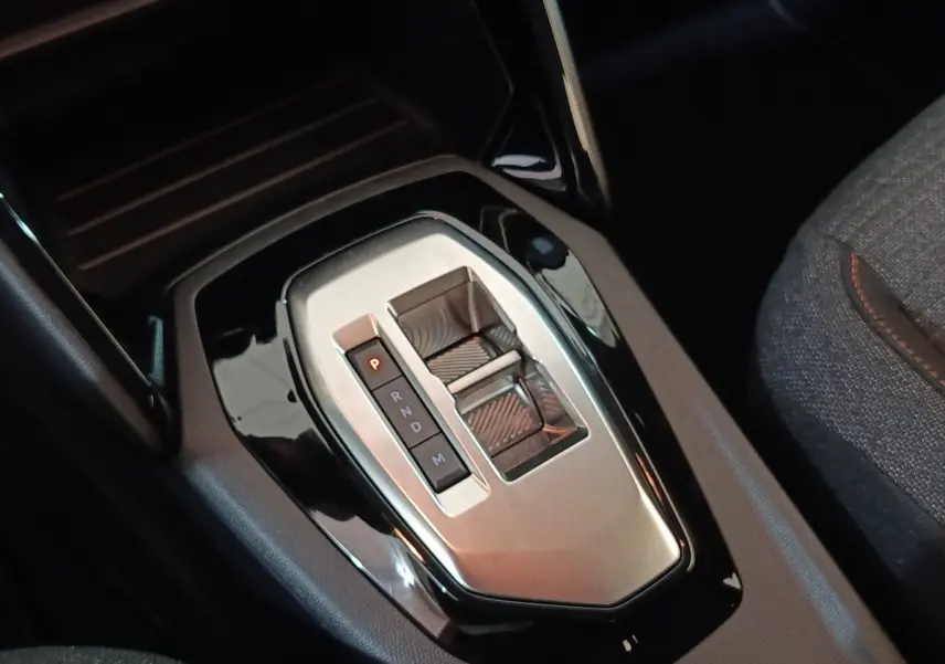 Gros plan sur la console centrale de la Peugeot 208 Hybrid 2025, avec levier de boîte automatique gris et noir.