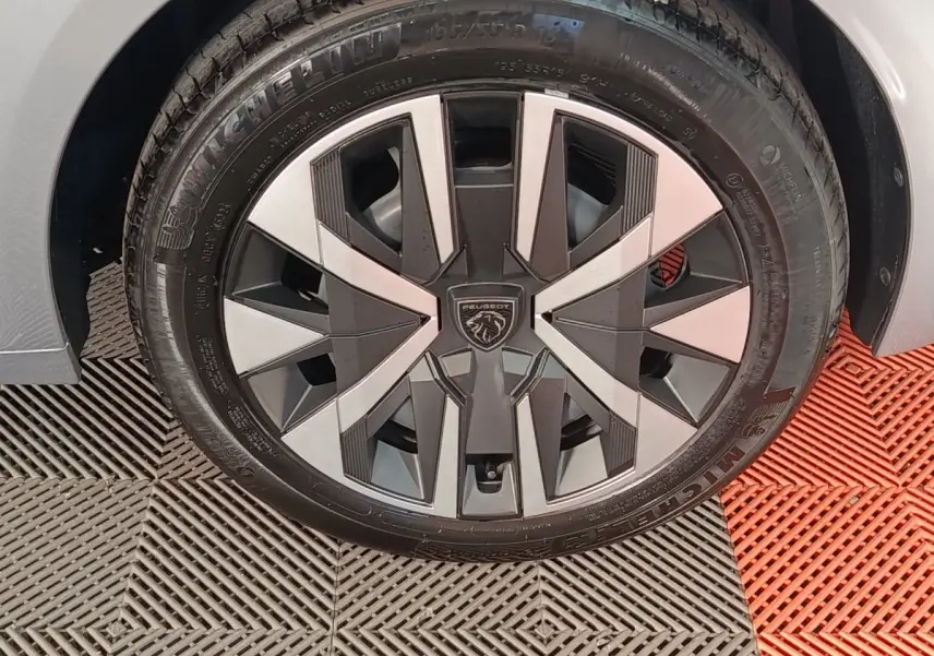 Gros plan sur la roue avant gauche avec jante stylisée bi-ton gris et noir de la Peugeot 208 Hybrid 2025 gris clair.