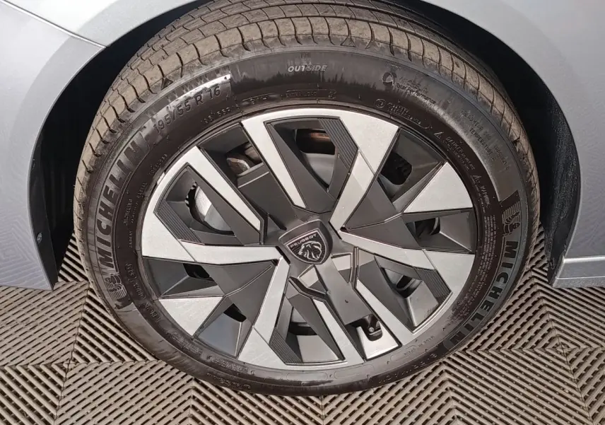 Gros plan sur la roue avant droite gris clair de la Peugeot 208 Hybrid 100 e-DCS6 avec jante en alliage au design géométrique.