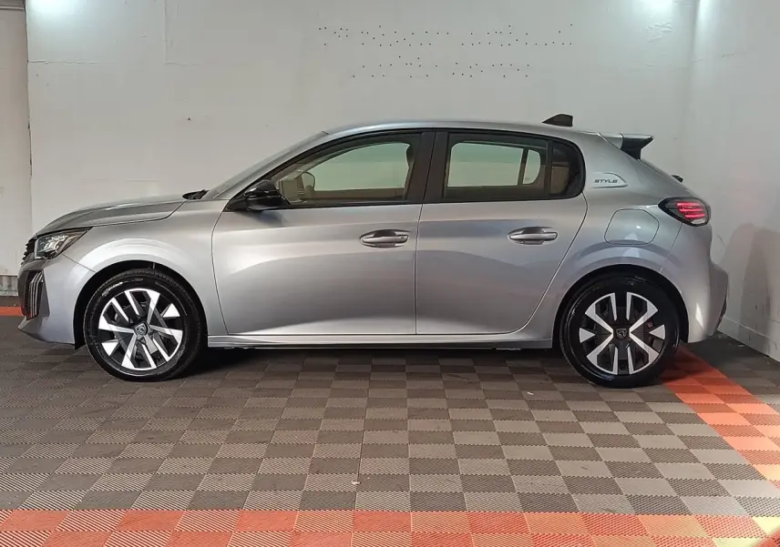 Profil latéral droit de la Peugeot 208 Hybrid gris clair 2025 avec jantes alliage et badge Style sur l'aile arrière.